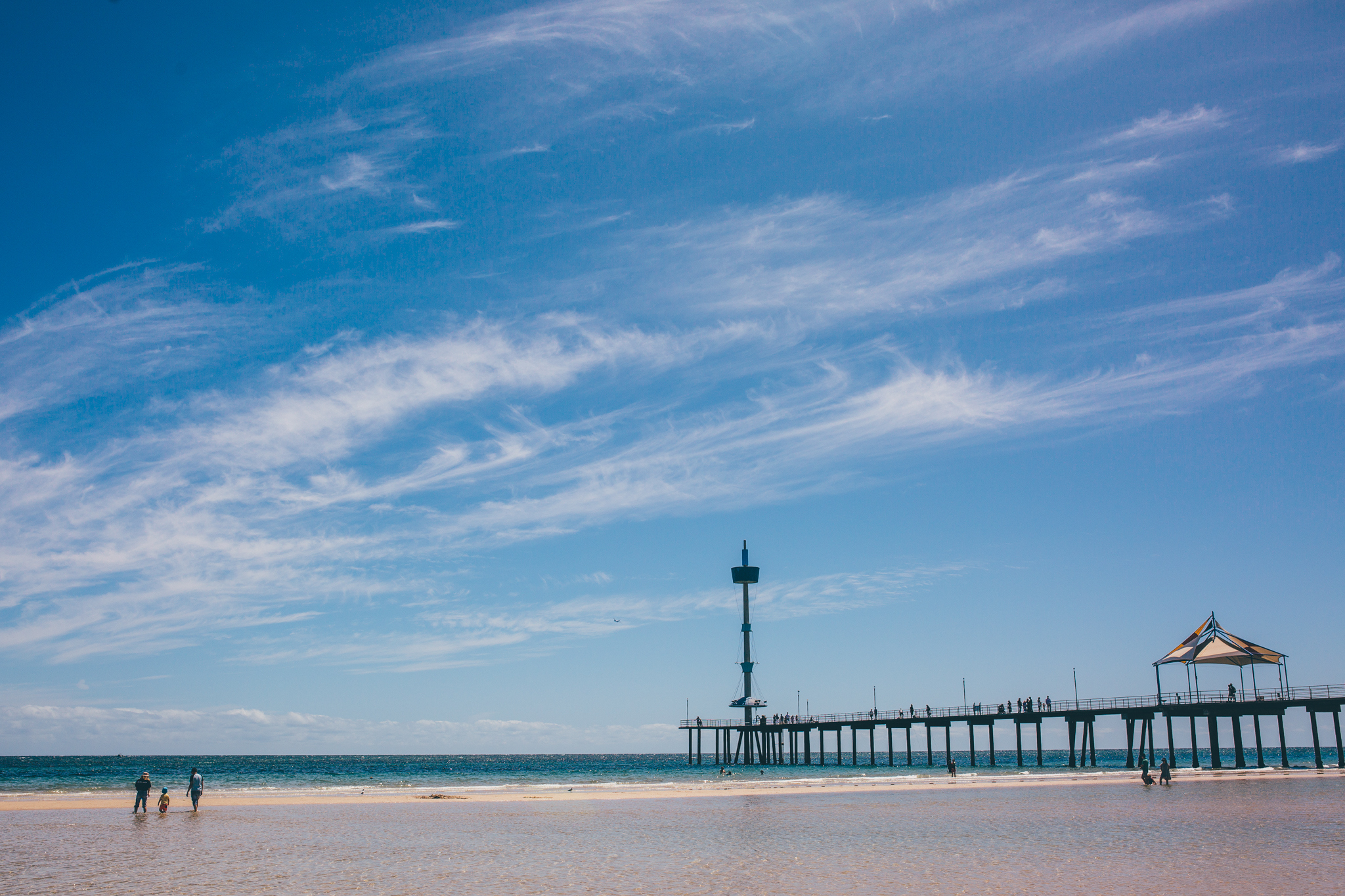 Brighton Jetty, against a blue sky, sand and ocean can be seen amongst jetty in the distance