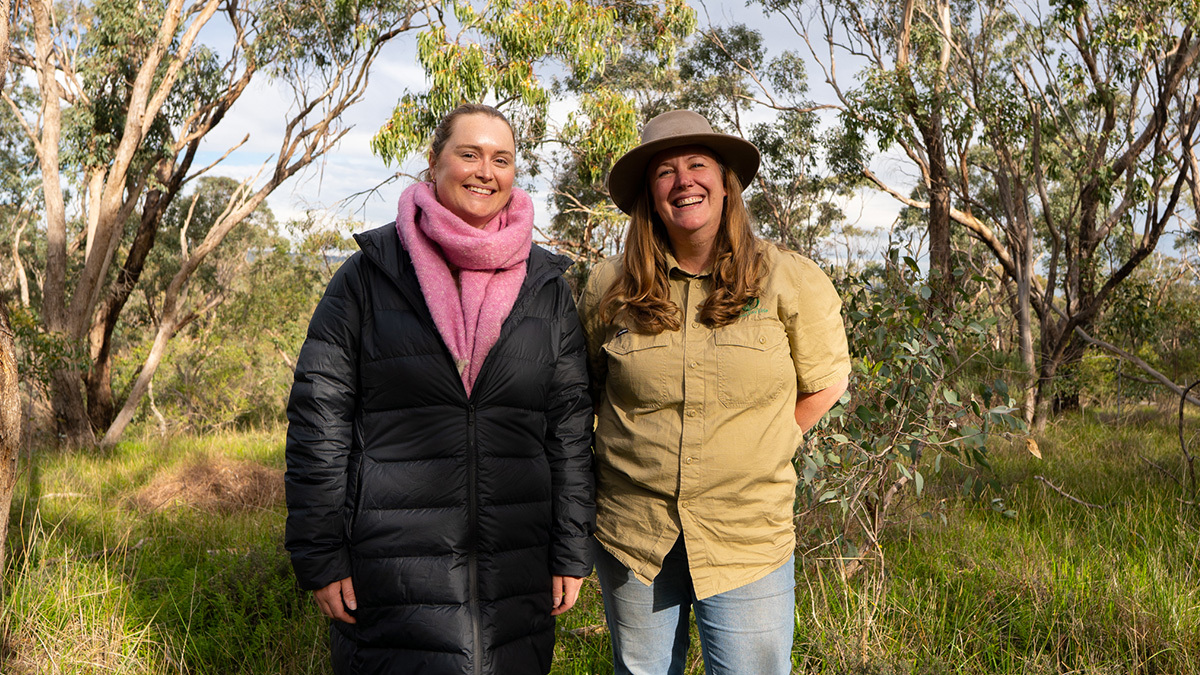 Two people standing in front of a grassy woodland in Adelaide.