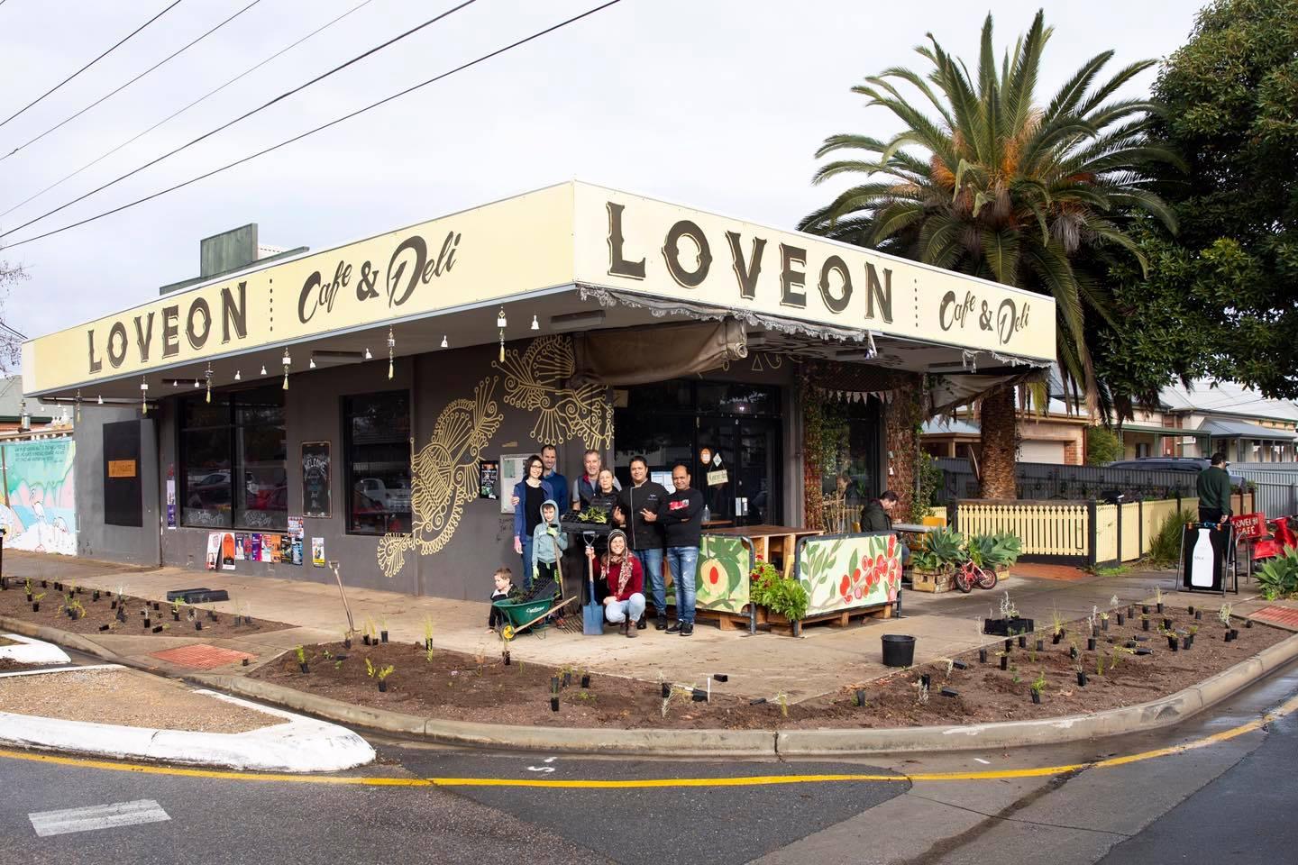 A group of people stand in front of the Loveon cafe and around newly planted street verges