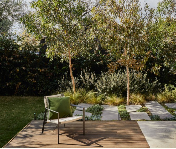 A shallow deck and chair over green garden with large stepping stones, native trees and shrubs. Garden design by Peachy Green.