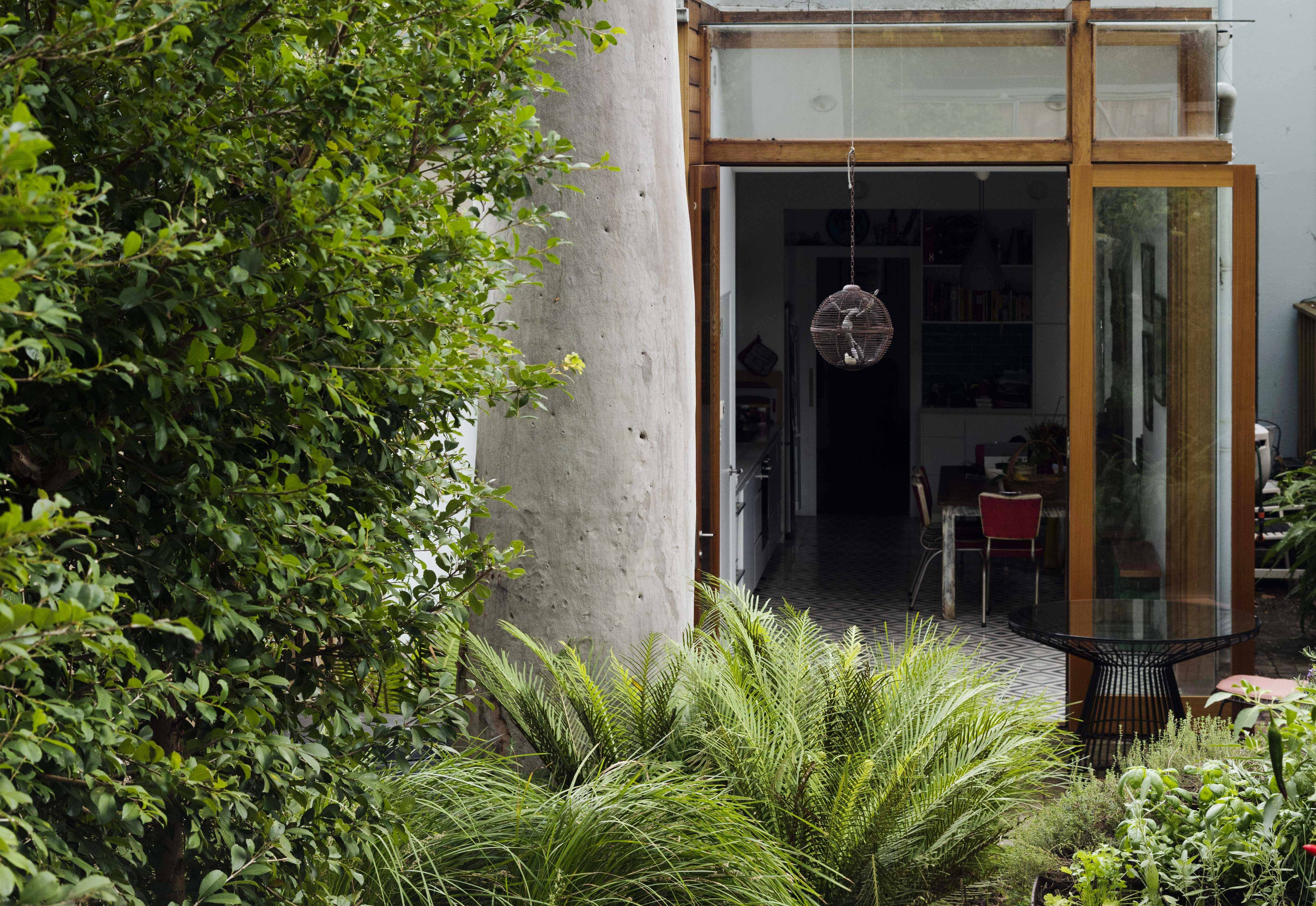 Glass doors of a house open out to a lush green backyard with a large, established tree.