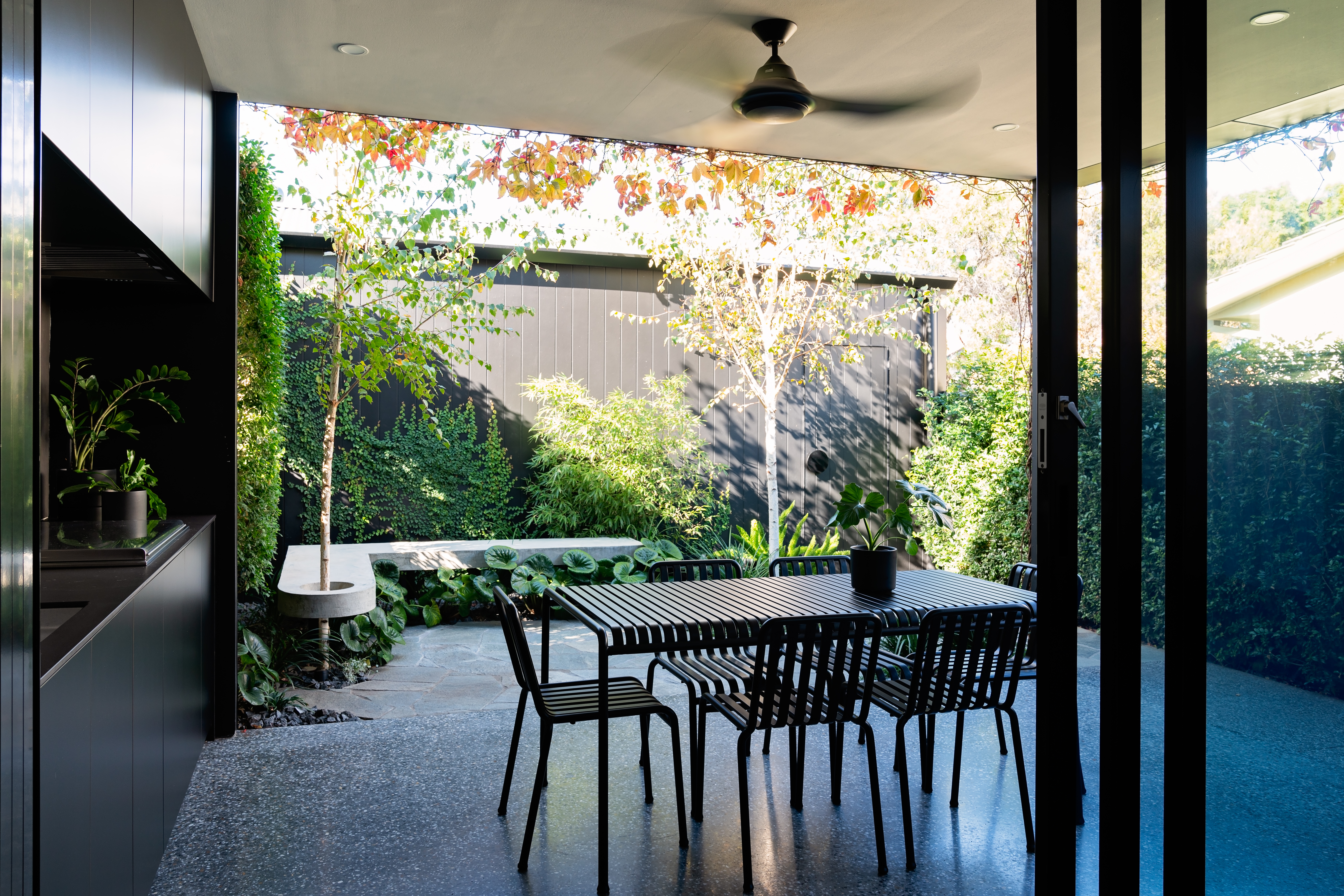 Table and chairs in outdoor setting in front of leafy small garden with stone bench and fence, Somerton Park, Landscape Techniques, Brad Griffin Photography 1