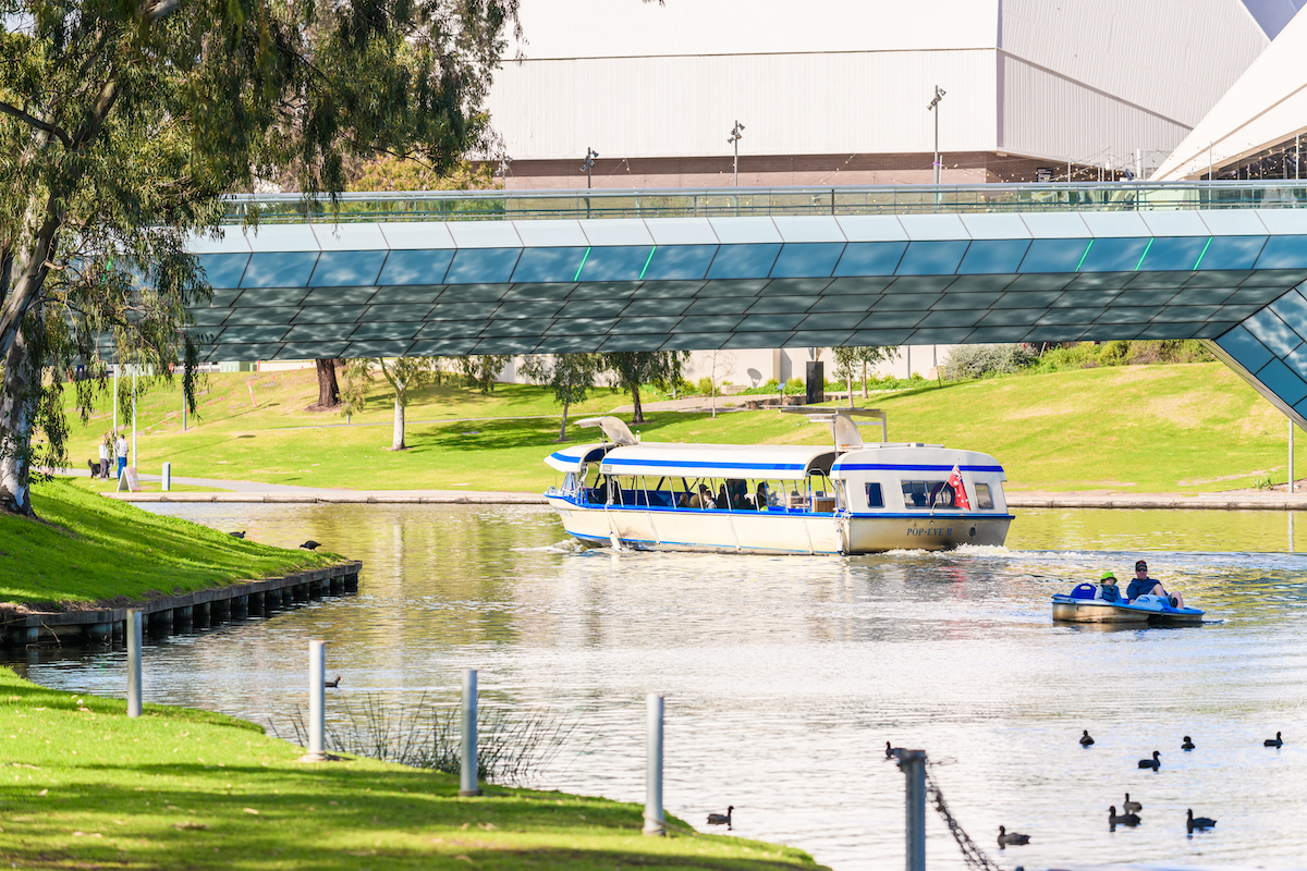 A photo of Torrens Lake with the Popeye boat travelling under the footbridge and a paddleboat can be seen in the shot