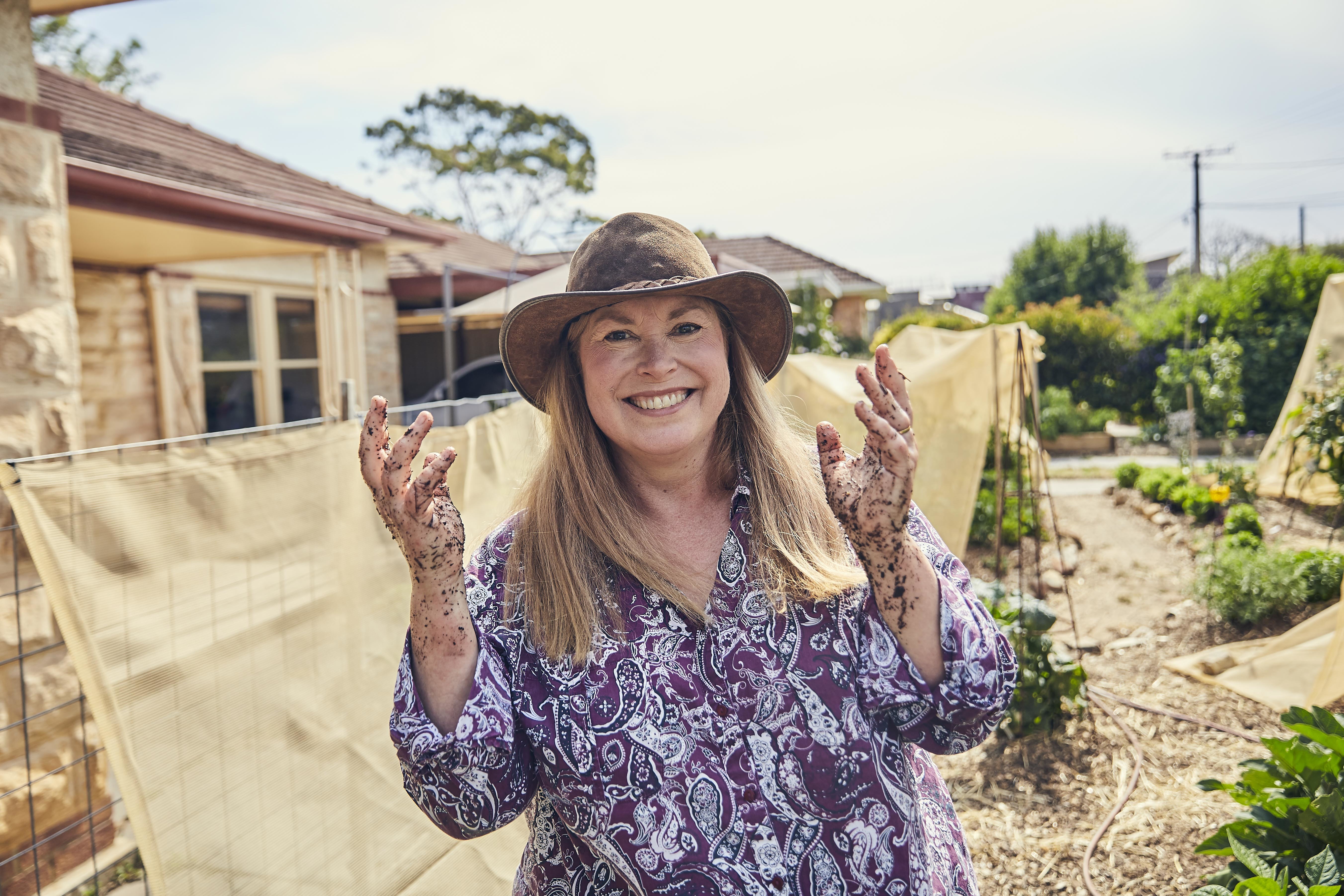 A smiling woman holding up dirty hands from gardening.